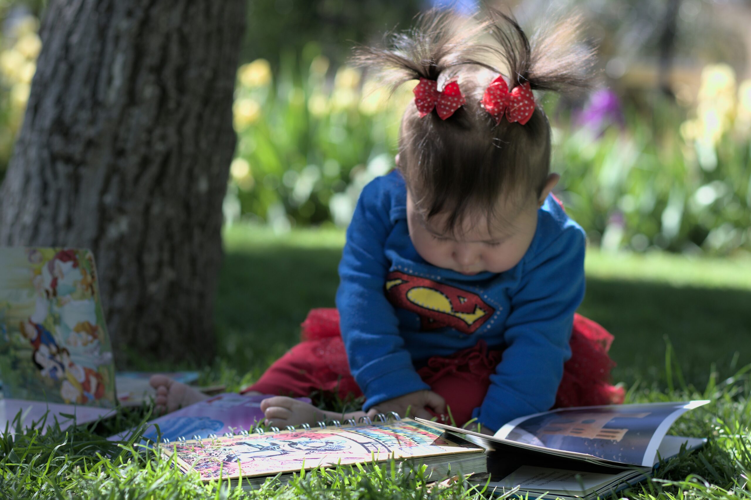 Niña leyendo libros en el jardín con camiseta de superhéroe